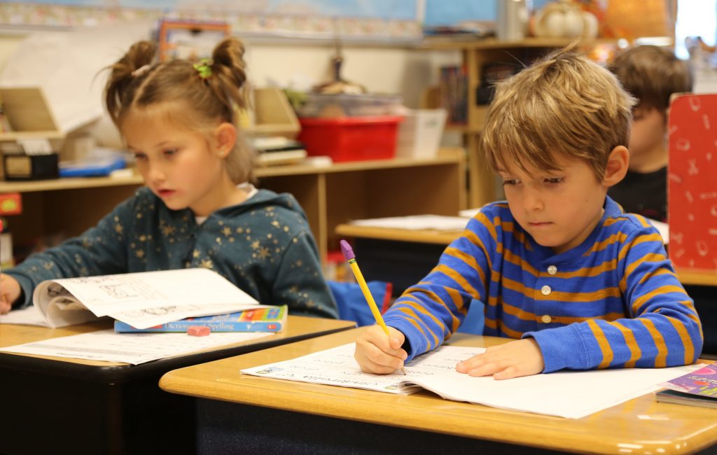 two students seated at desks writing